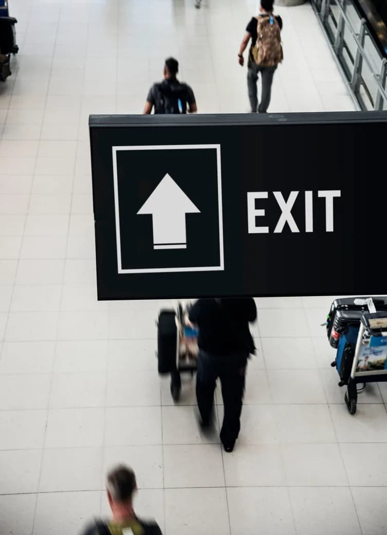 Travelers walking beneath an exit sign in an airport concourse