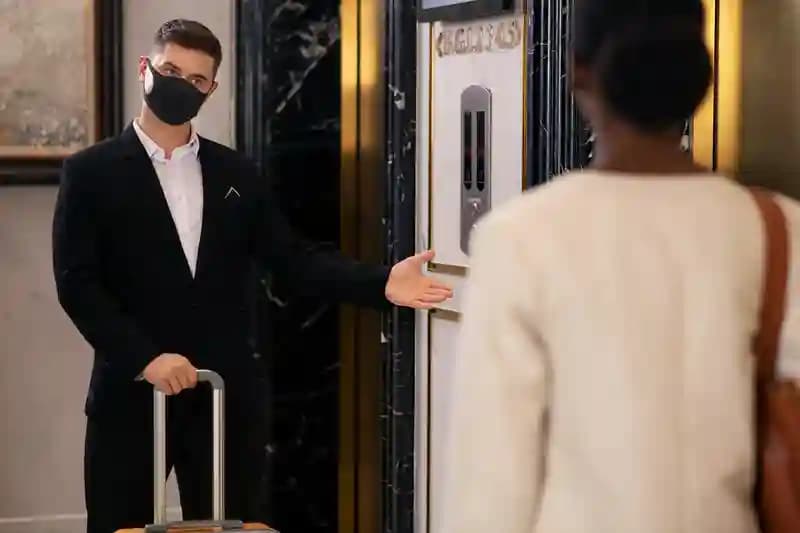 A porter holding a suitcase and gesturing a guest through a doorway