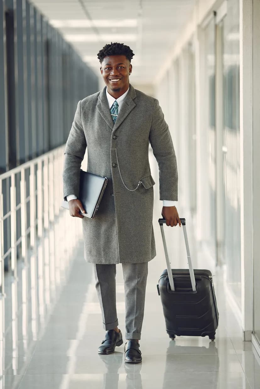 A traveler in an overcoat walking a terminal corridor with a suitcase