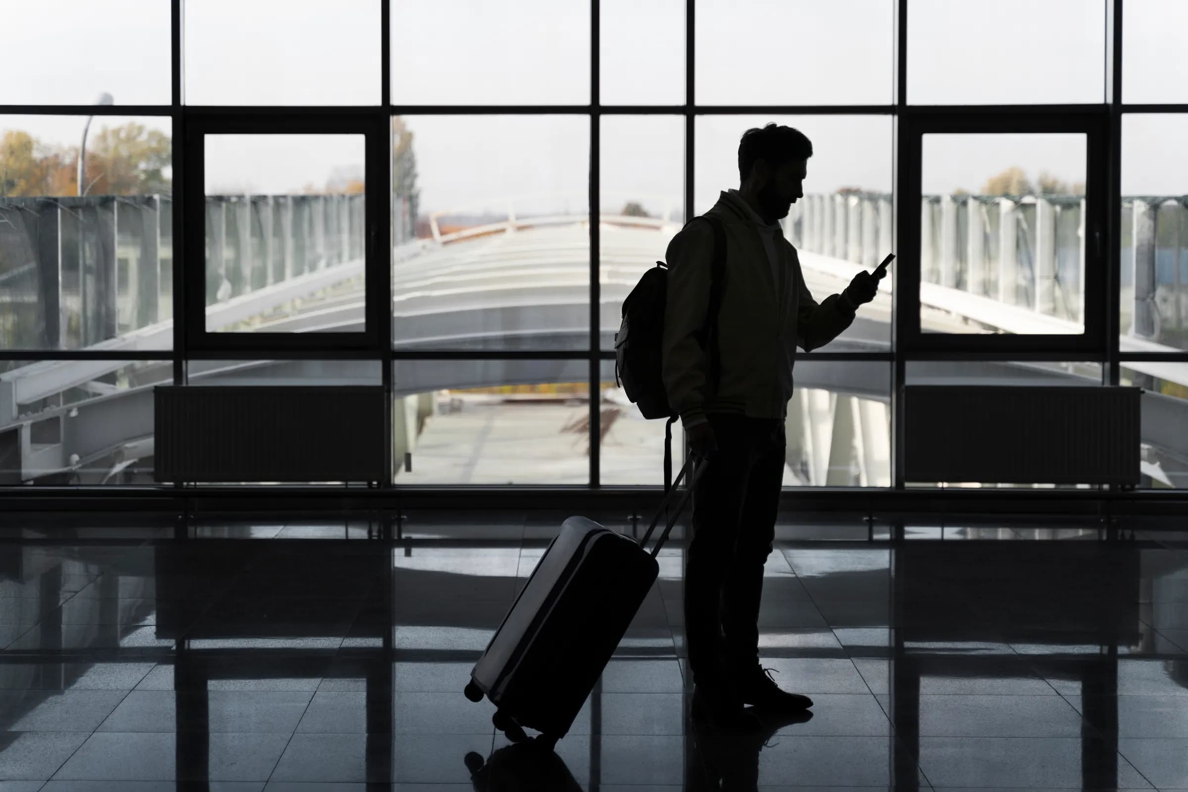 A traveler with a suitcase waiting beside a terminal window before departure